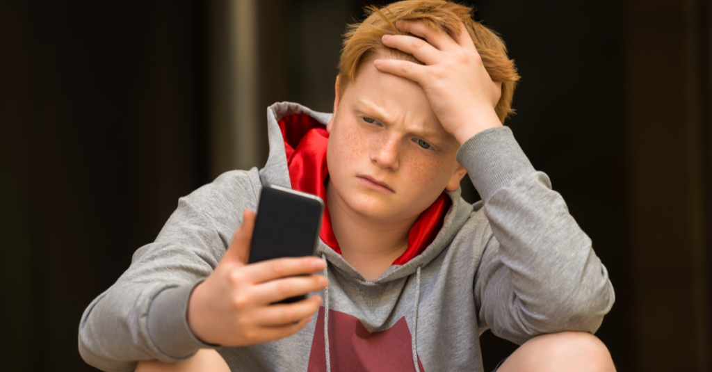 Chłopiec z ręką na głowie patrzeje zmieszany przy jego telefonem