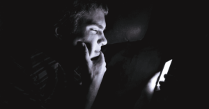 A teen looks at their bright phone in the dark.