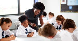 Uma professora sorri e ajuda um grupo de alunos que trabalha em sua mesa.