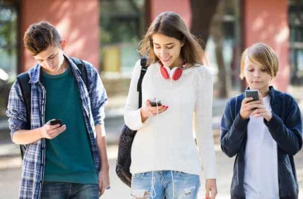 Três crianças de diferentes idades potencialmente usando mídias sociais em seus smartphones.