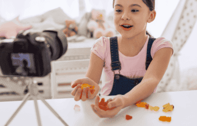 Un bambino piccolo con una macchina fotografica su un treppiede, live streaming o vlog con i dolci.