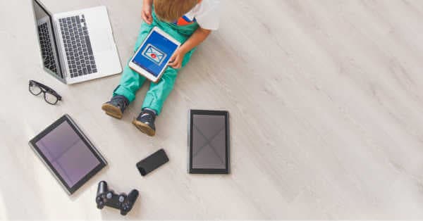 एक बच्चा फर्श पर विभिन्न तकनीकी उपकरणों का उपयोग करता है।
