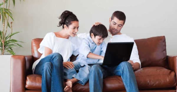 Uma mãe e um pai olham para um laptop com seu filho.