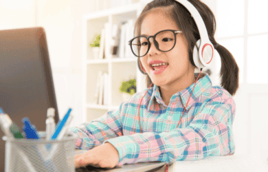 Kleines Mädchen mit Kopfhörern beim Sitzen auf einem Schreibtisch auf einem Laptop