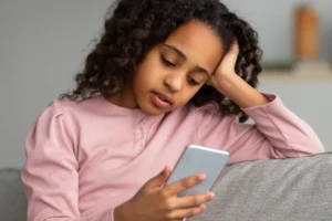 一个年轻女孩坐在沙发上看着她的智能手机。