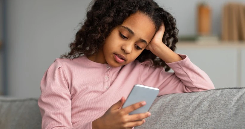 Una giovane ragazza è seduta sul divano e guarda il suo smartphone.