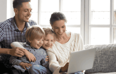 Familie van vier die op bank zitten die bij laptop glimlachen