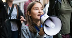 A young girls speaks into a megaphone within a crowd.