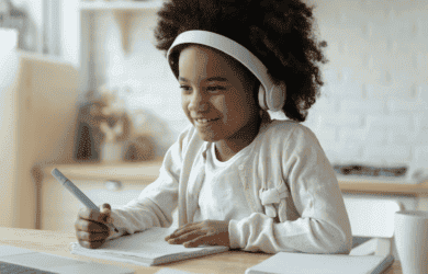 Child on laptop with pen and paper and headphones on