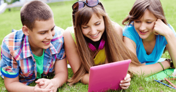 Tres adolescentes usan una tableta mientras pasan tiempo al aire libre, combinando actividades en línea y fuera de línea.