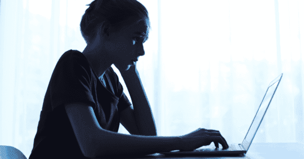 A pre-teen browses a laptop in silhouette, with worried body language.