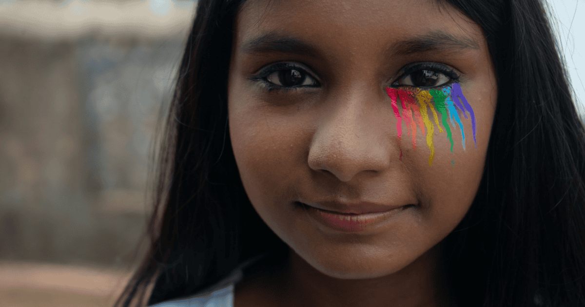 Close-up van het lachende gezicht van een jong meisje met regenboogkleuren voor LGBT die onder haar linkeroog loopt.