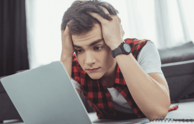 Teen boy holds his head and looks concerned as he looks at his laptop.