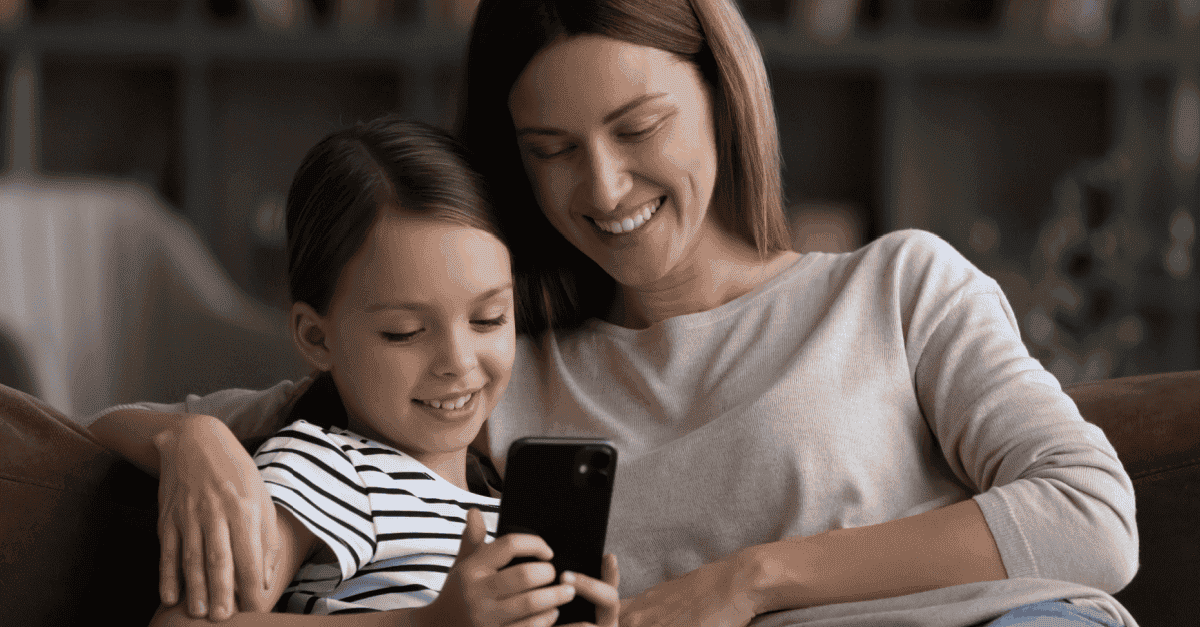 Mother supporting her child in a digital world through looking at a smartphone together, smiling.