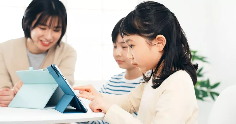 一位妈妈和她的两个孩子坐在一起，他们正在平板电脑上观看视频，可能是通过 YouTube 或 YouTube Kids 观看的。