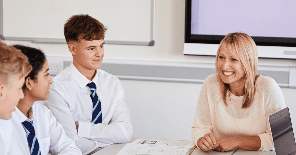 एक महिला शिक्षक 3 किशोर छात्रों के साथ काम की मेज के चारों ओर मुस्कुरा रही है