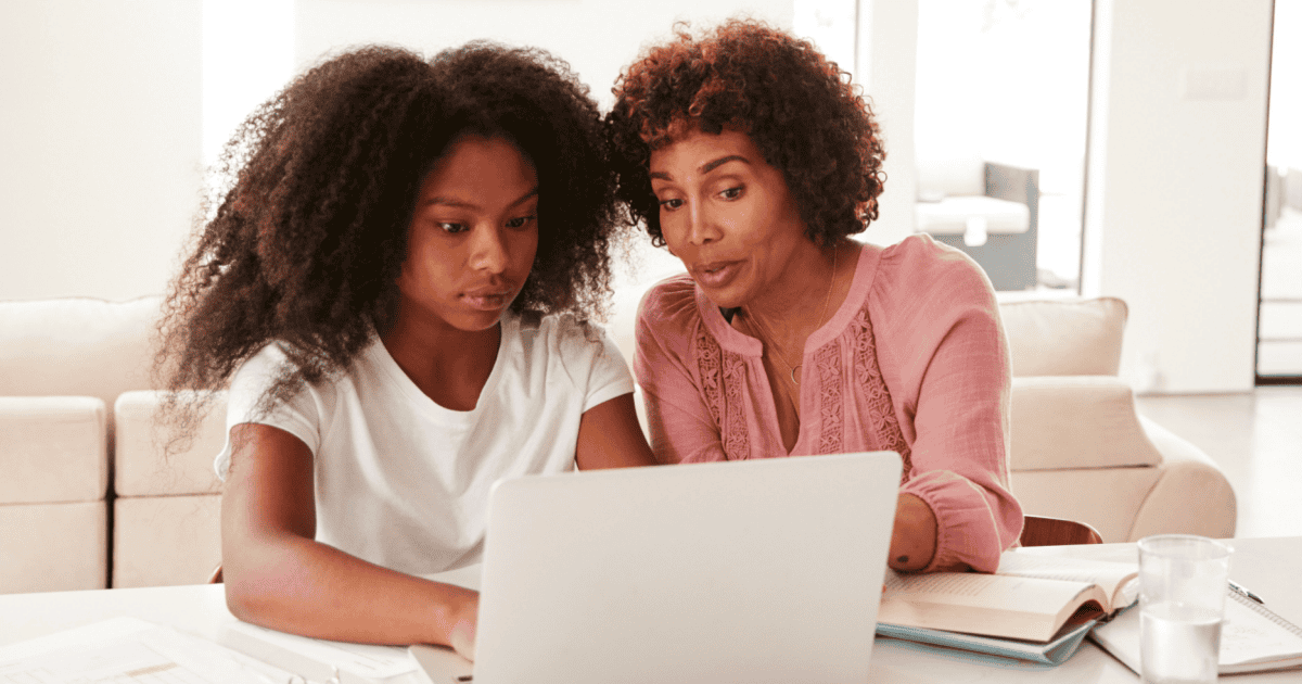 Mamá mostrando a su hija adolescente algo en su computadora portátil como si explicara las estafas en línea comunes dirigidas a los adolescentes