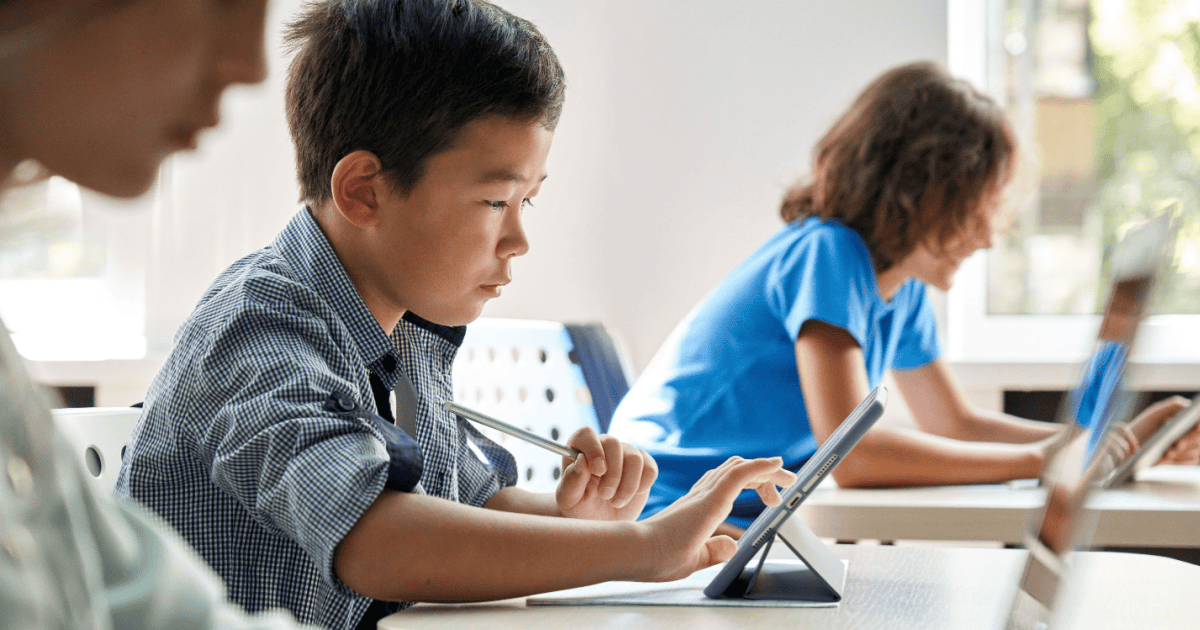 A pre-teen boy works on a tablet with other children working in the background and foreground. The Ofcom response looks at keeping children like them safe online.