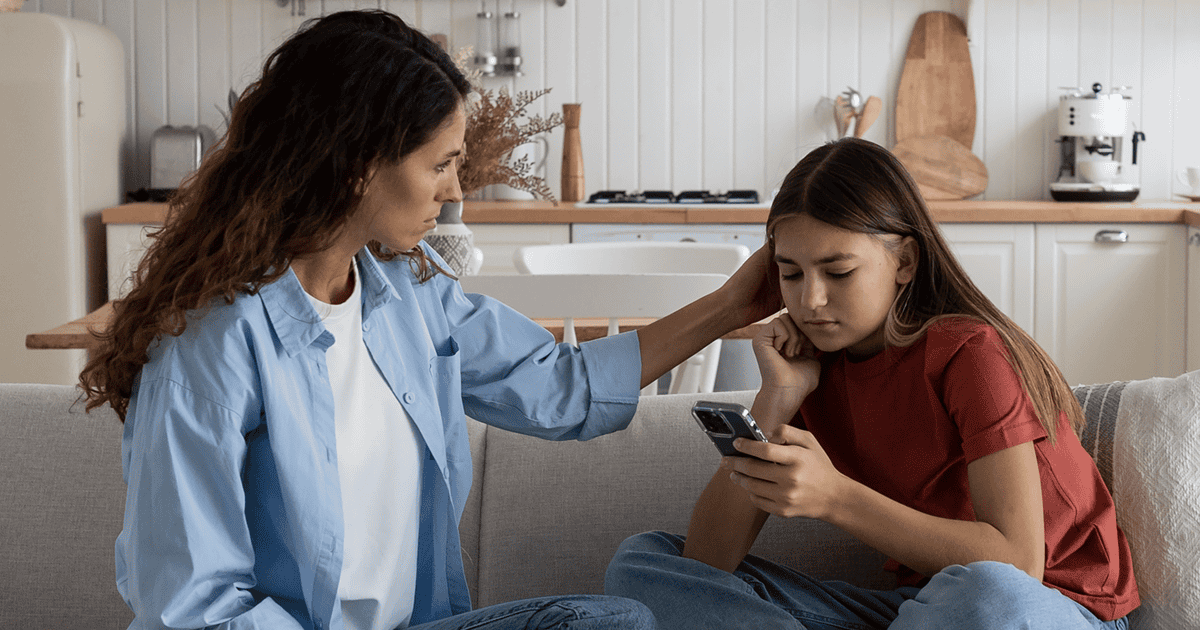 A mum comforts her daughter who looks upset as she stares at her smartphone.