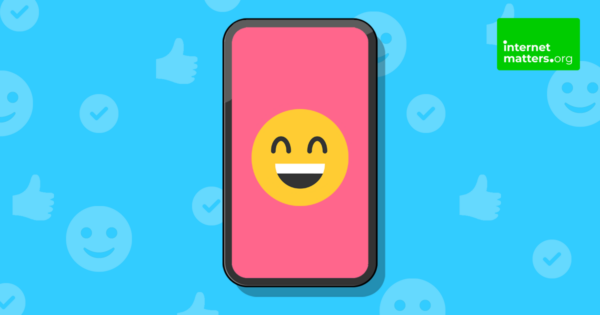 Obraz smartfona przedstawiający wesołą emotikonę na tle z pozytywnymi ikonami symbolizującymi rozrywkę dla dzieci.