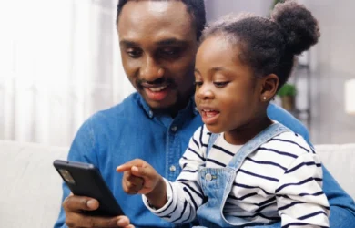 Ojciec patrzy na smartfona z córką, ważną częścią cyfrowego bezpieczeństwa oprócz kontroli rodzicielskiej.