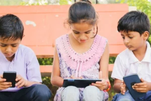 Ein Foto zeigt drei Kinder, die draußen sitzen und Geräte benutzen. Die Auswahl der richtigen Apps kann das Wohlbefinden und eine ausgewogene Bildschirmzeit unterstützen.