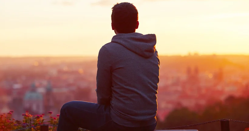 Un niño sentado contemplando una puesta de sol sobre una ciudad, la imagen que aparece en el informe Niños vulnerables en un mundo digital.