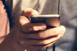 Uma imagem aproximada de uma mão segurando um smartphone, possivelmente navegando nas redes sociais.