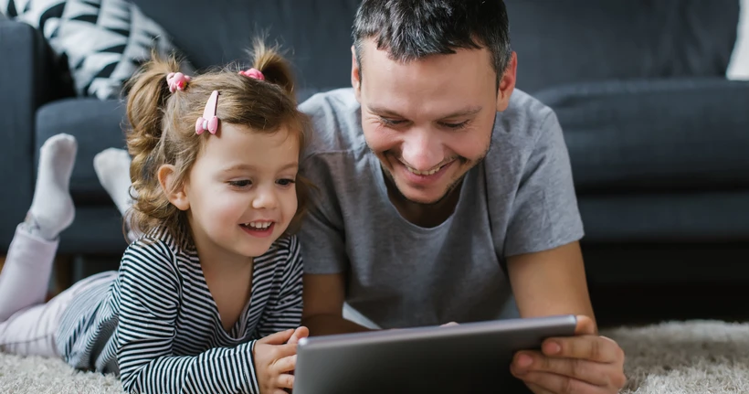 A dad and toddler play on a tablet, laughing.