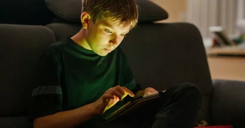 Chłopiec spędza czas przed ekranem tabletu, a światło odbija się na jego twarzy.