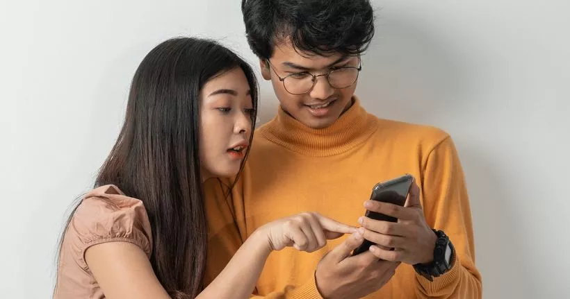 Dos adolescentes miran un teléfono inteligente.