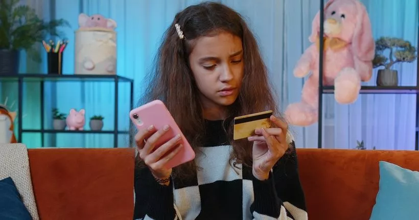 A teen looks at a credit card while holding a smartphone.