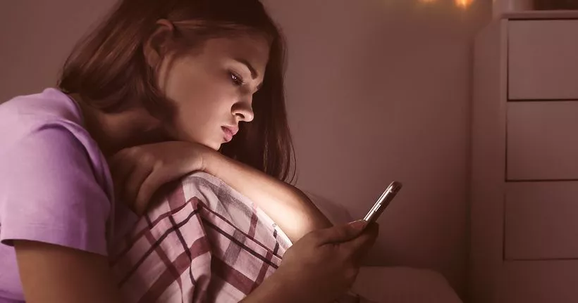 A teen looks at their smartphone in their bedroom.