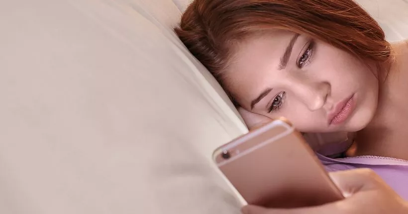 一名青少年在床上使用手机。
