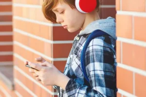 Ein Kind trägt Kopfhörer und nutzt ein Smartphone.