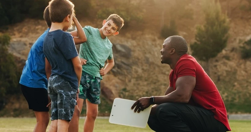 Ein Trainer geht in die Hocke, während er mit den Jungen spricht, die er trainiert.