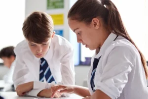 Een jongen en een meisje in uniform, aan het werk in een klaslokaal op school.
