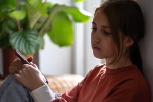 Ein Mädchen sitzt mit traurigem Gesichtsausdruck vor ihrem Telefon.