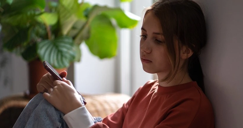 Ein Mädchen sitzt mit traurigem Gesichtsausdruck vor ihrem Telefon.