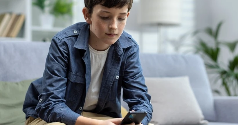 A boy sits, using a smartphone.