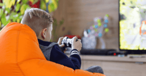 A boy sits in front of a TV with a games controller, playing video games.
