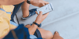 A man sitting on a bench holding a smartphone with his two hands