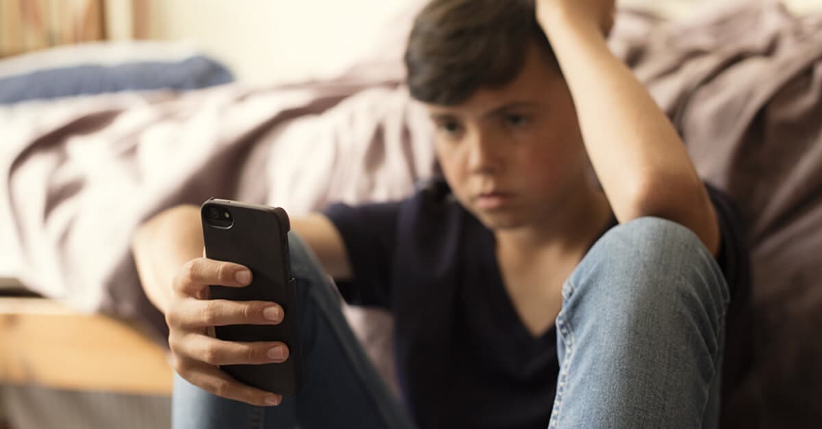 A boy looks at his smartphone, upset.