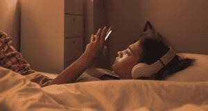 A teen wears headphones, lying down while they look at their phone.