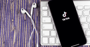 A smartphone with headphones on a computer keyboard. The phone shows the TikTok logo.