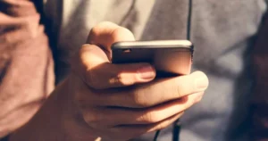 A close up image of a hand holding a smartphone, possibly scrolling social media.