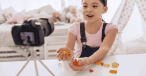 A young child with a camera on a tripod, live streaming or vlogging themselves with sweets.