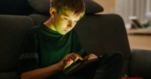 A boy spends his screen time on a tablet with the light reflecting on his face.