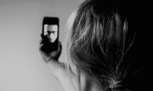 A person holds a smartphone in front of them with a person on screen.