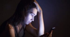 A teen sits in the dark with their smartphone illuminating their face.